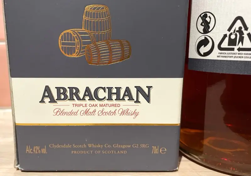Elegancka butelka Abrachan Blended Malt Scotch Whisky, potrójnie dojrzewająca w dębie, z beczkami na etykiecie.