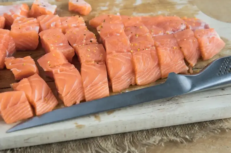 Pokrojony łosoś, idealny jaki łosoś do sushi, leży na desce obok noża.