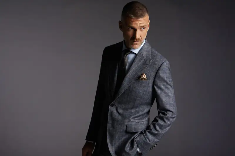Elegancki mężczyzna w garniturze w kratę. Czy to Dressmann? To firma oferująca modną odzież męską.