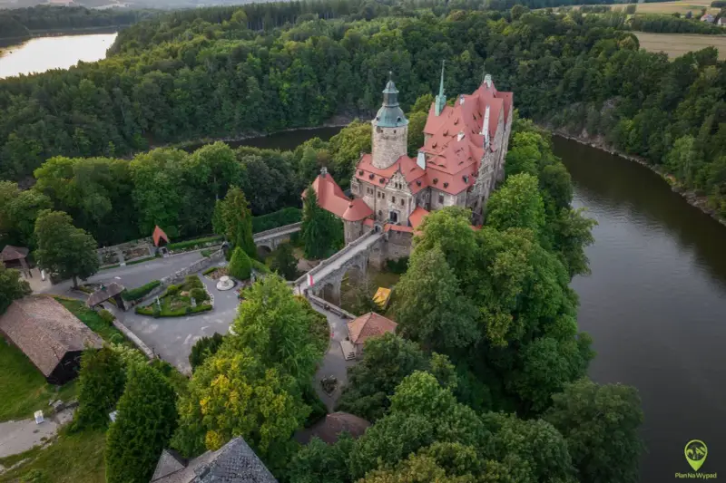 Zamek Czocha, malowniczo położony na skalistym cyplu nad rzeką, otoczony bujną zielenią.