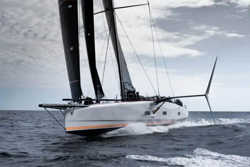 Le voilier Baltic 111 Raven fend les vagues, ses voiles noires gonflées par le vent.