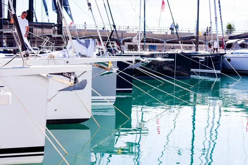 Des voiliers modernes, prêts à prendre la mer, sont amarrés dans un port. Leurs proues blanches et leurs ancres visibles rappellent le cale bateau.