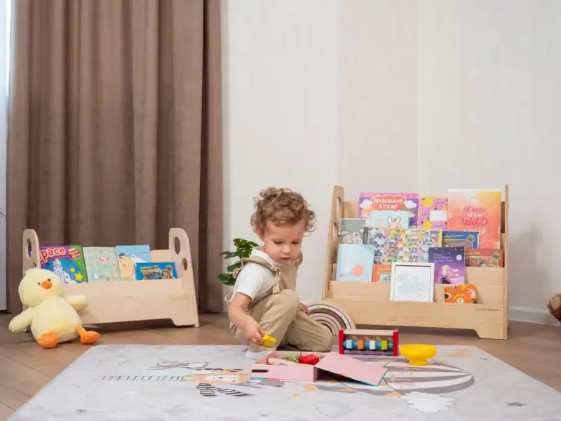 Kleines Kind spielt mit Holzspielzeug vor einem Regal mit Büchern, das eine Sitzordnung im Montessori-Stil widerspiegelt.