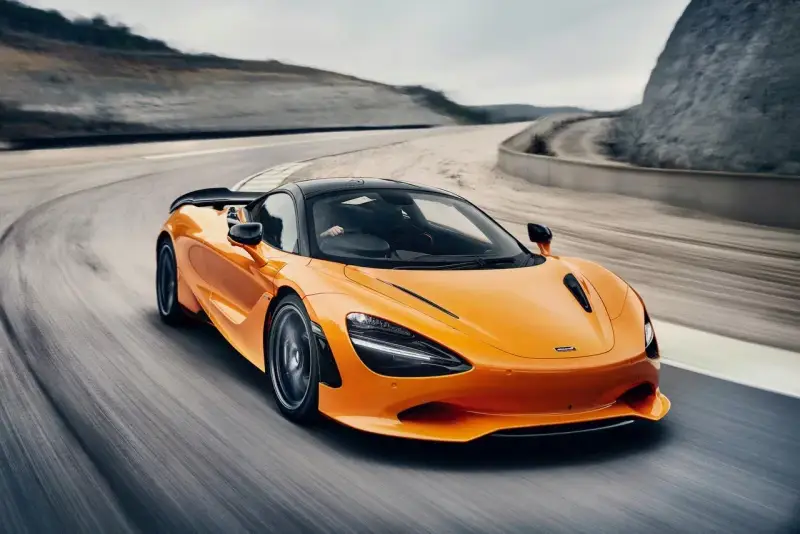 Pomarańczowy McLaren 750S z czarnym dachem sunie po torze wyścigowym, tworząc dynamiczny obraz prędkości i mocy.