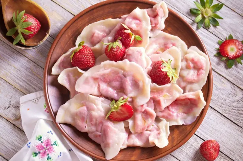 Pyszne pierogi z truskawkami, ozdobione świeżymi owocami, wyglądają apetycznie na glinianym talerzu.