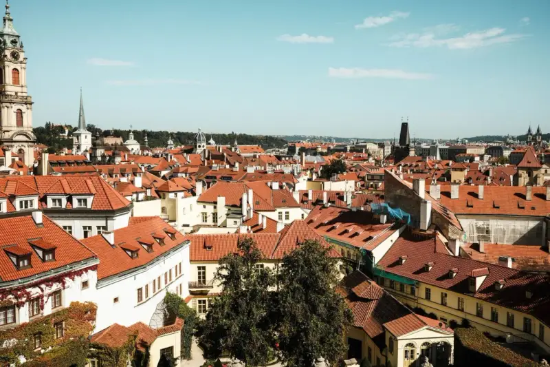 Widok na dachy Pragi, idealne miejsce na tani city break. W oddali wieże i kopuły.