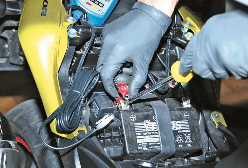 Mani guantate collegano un mantenitore di carica moto sempre collegato alla batteria.