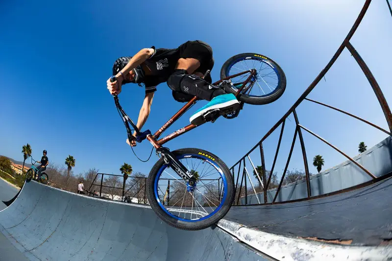 A BMX rider, possibly Chelsea Wolfe, performs a trick on a ramp against a clear blue sky.