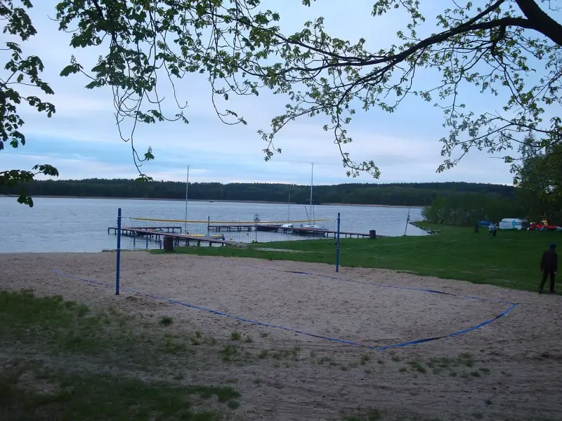 Plaża z boiskiem do siatkówki plażowej nad jeziorem w Borneńskim Sulimowie. W tle pomosty, żaglówki i las.