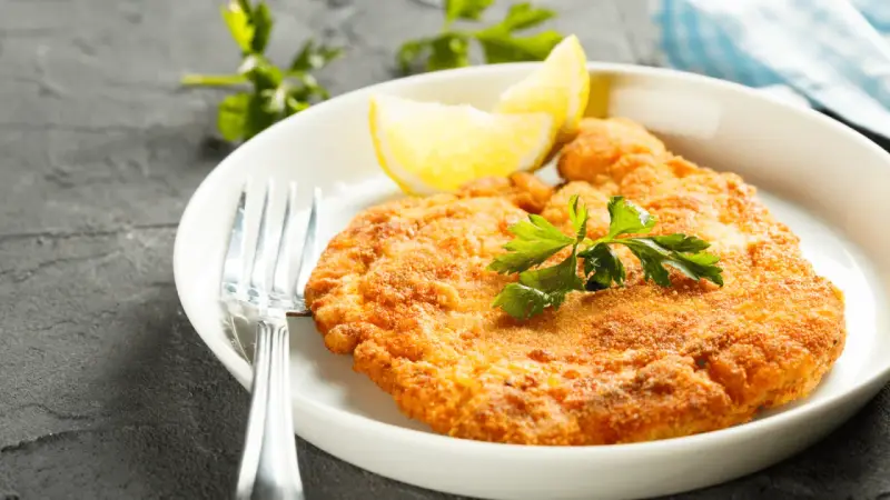 En gyllene schnitzel med citronklyfta och persilja, redo att avnjutas med ett glas vin till schnitzel.