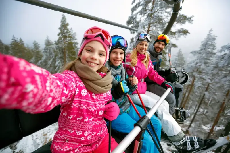 Rodzina na wyciągu narciarskim, robiąca selfie. Dziewczynka z przodu uśmiecha się szeroko. To ich wymarzone wczasy pod gruszą, ale zimowe!