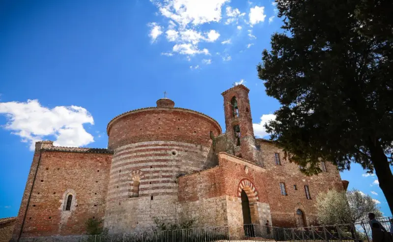 L'abbazia di San Galgano, con la sua rotonda in mattoni a fasce bianche e rosse, si staglia sotto un cielo azzurro con nuvole bianche.
