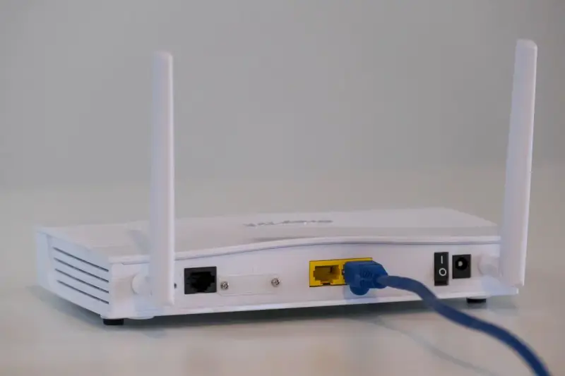 Biały modem z dwiema antenkami, podłączony niebieskim kablem Ethernet. To urządzenie, które pozwala na połączenie z internetem.