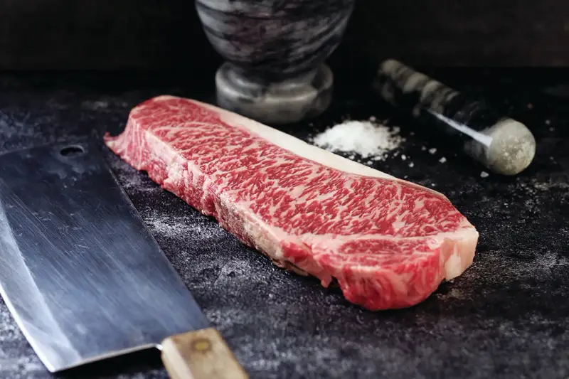 Wyjątkowy stek z krowy wagyu, gotowy do przygotowania. Obok nóż i moździerz z solą.