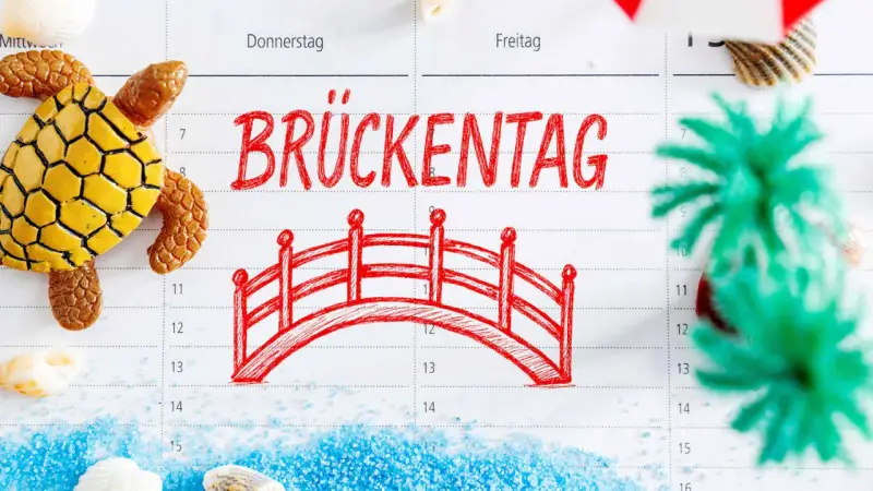 Kalenderblatt mit "Brückentag" und einer roten Brücke, Schildkröte, Muscheln und Dekoration.