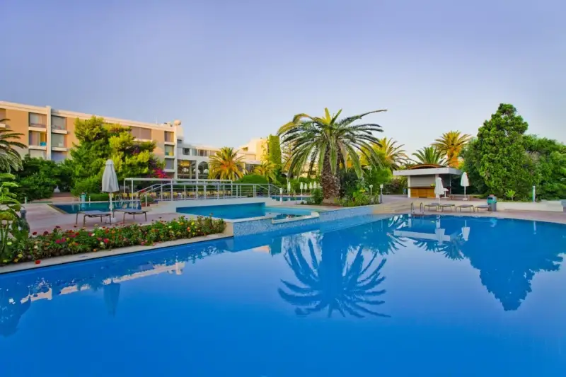 Basen hotelowy z palmami i kwitnącymi kwiatami, idealne miejsce na relaks przy Caravia Beach Kos.