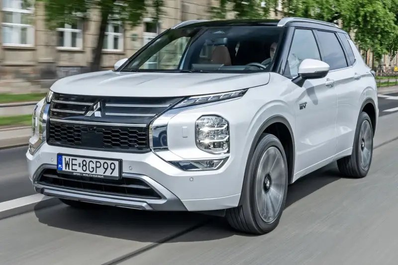 Biały Mitsubishi Outlander PHEV, jeden z nowoczesnych modeli tej marki, jedzie po mieście.