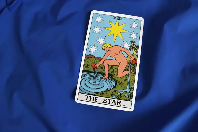 Karta XVII - Gwiazda Tarot. Kobieta wylewa wodę z dzbanów do stawu, symbolizując nadzieję i odnowę.