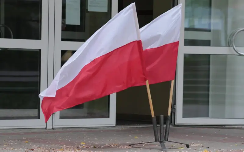 Dwa polskie flagi przed budynkiem. Dowiedz się, jak głosować za granicą, by Twój głos miał znaczenie.