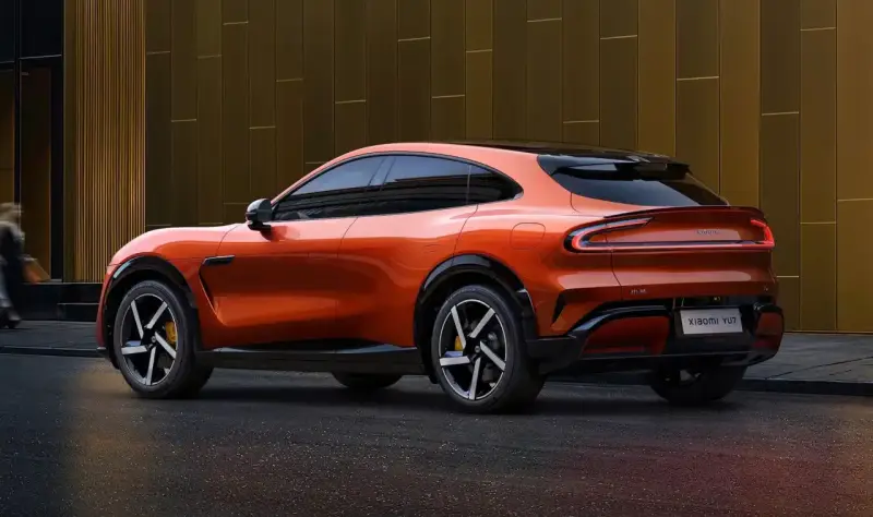 La **Xiaomi car** orange vif, un SUV coupé futuriste, se gare devant un bâtiment moderne aux reflets dorés.