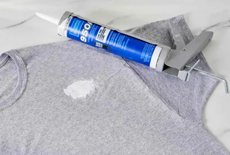 Zaschnięty silikon na szarym T-shircie i pistolet do jego aplikacji. Dowiedz się, jak usunąć zaschnięty silikon z ubrania.