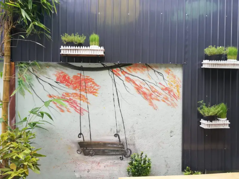 Un columpio pintado en un muro, ideal para inspirar al pintar patios pequeños. Las ramas anaranjadas y el bambú añaden color.