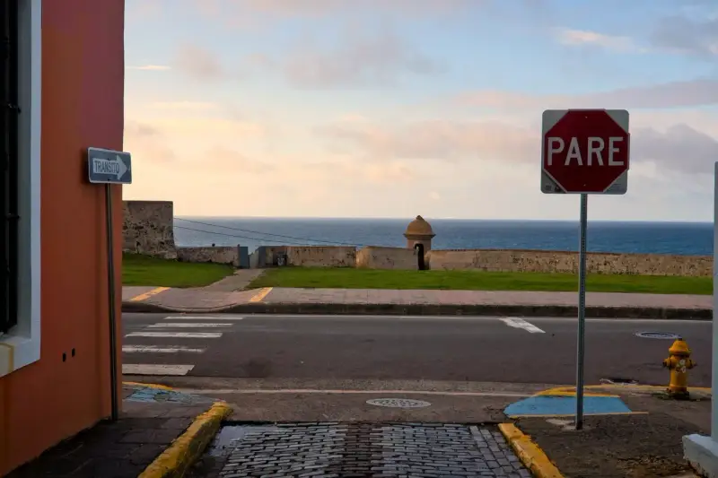 A "PARE" sign stands by the ocean in Puerto Rico. Should I rent a car to explore this beautiful island?