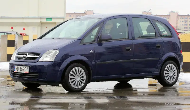 Granatowy Opel Meriva na mokrej nawierzchni. Kierowca w okularach. Wiele pozytywnych opinii o tym modelu.