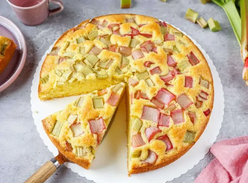 Saftiger Rhabarberkuchen, ein Klassiker unter den Rezepten mit Rhabarber. Ein Stück wird gerade herausgehoben.