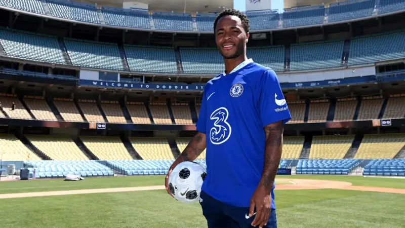 Raheem Sterling w niebieskiej koszulce Chelsea z piłką, na tle stadionu. Jego statystyki w klubie są obiecujące.