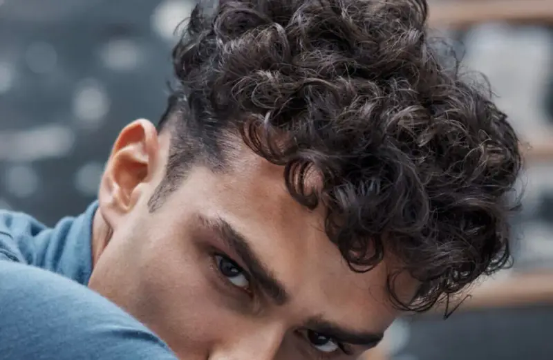 Gros plan sur un homme avec une coupe homme mi long bouclé, ses boucles sombres encadrant son visage.