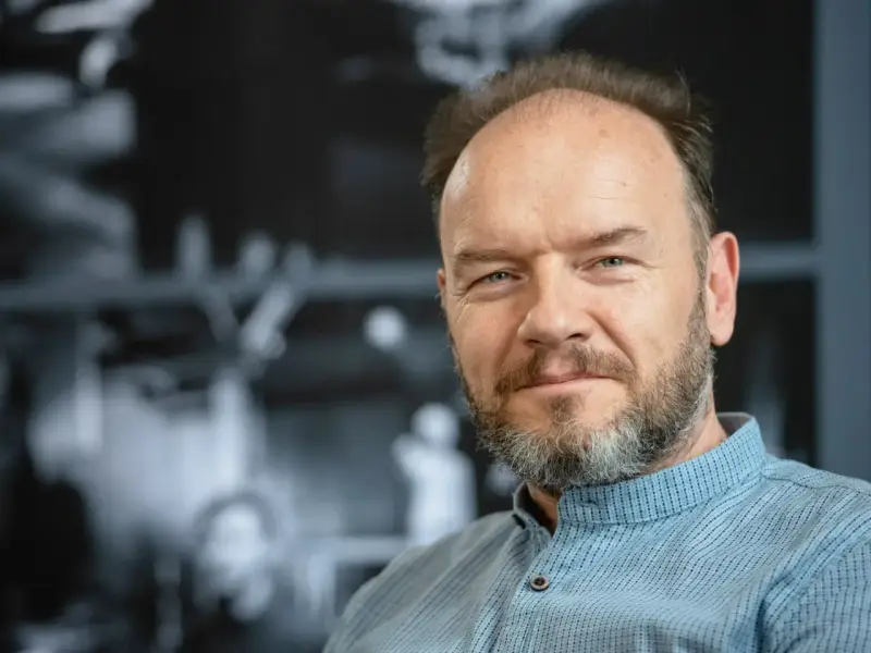 Portret mężczyzny z siwiejącą brodą, w niebieskiej koszuli. Redbad Klynstra dzieli się swoimi poglądami.