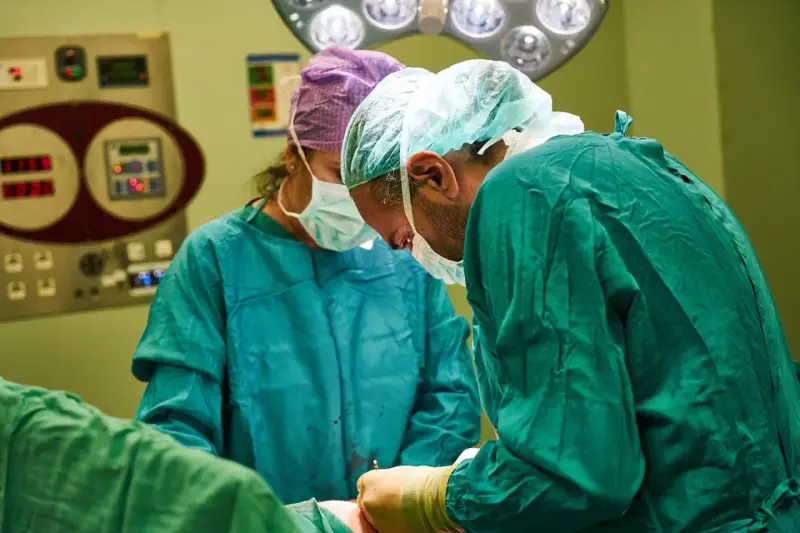 Chirurdzy w maseczkach i czepkach przygotowują się do operacji. Narkoza już działa, pacjent jest bezpieczny.