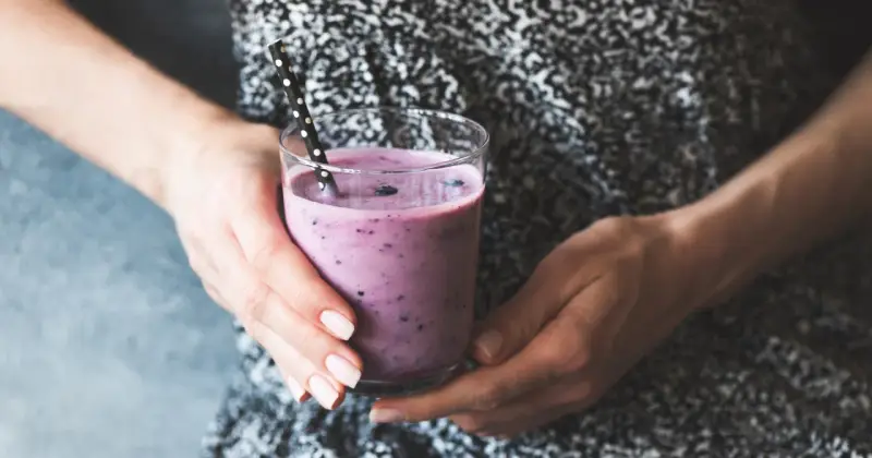 Ręce trzymają szklankę z fioletowym smoothie, które może być skuteczną miksturą na zaparcia.