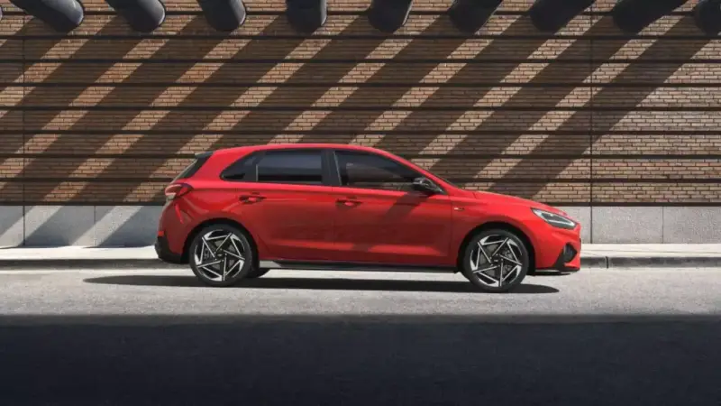 Czerwony Hyundai i30 stoi na tle ceglanej ściany z ciekawymi cieniami.