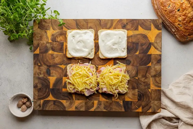 Przygotowanie croque madame: na kromkach chleba szynka i ser, na drugiej sos beszamelowy.