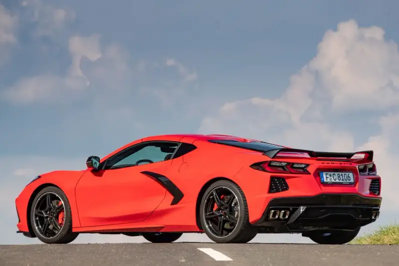 Czerwony Chevrolet Corvette C8 z czarnym spoilerem i felgami, zaparkowany na drodze pod błękitnym niebem z chmurami.