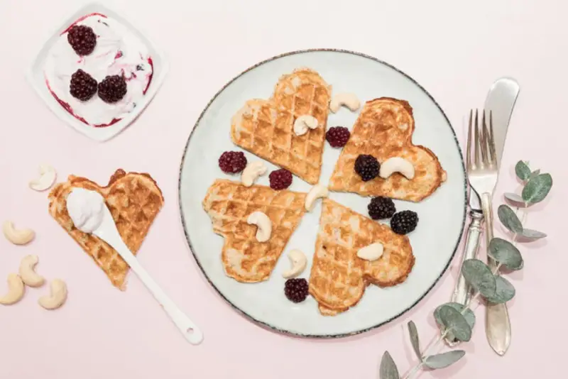 Hjärtformade protein våfflor med bär och cashewnötter. En skål med yoghurt och bär står bredvid.