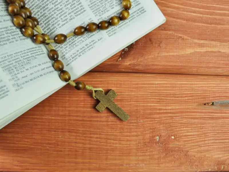 Różaniec na drewnianym stole obok Biblii, przypominający o 10 przykazaniach kościelnych i modlitwie.