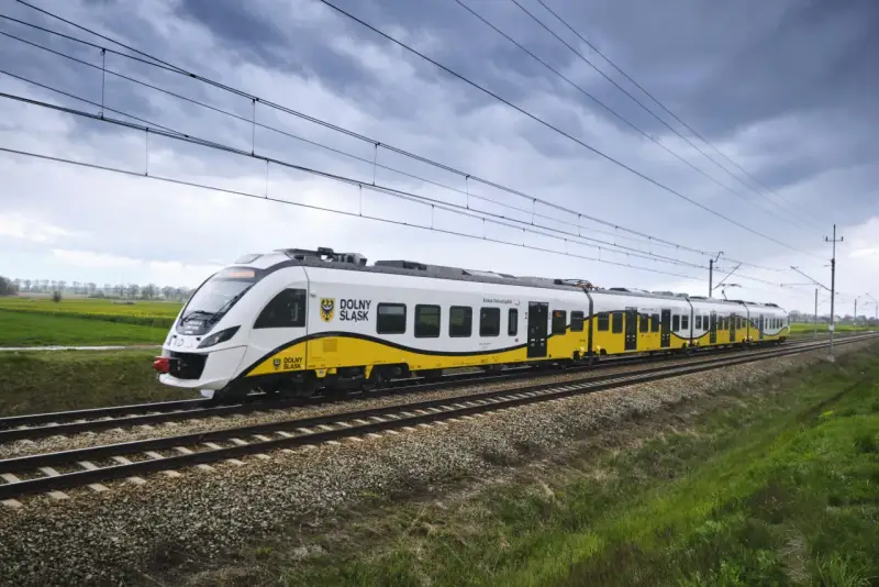 Pociąg Kolei Dolnośląskich z charakterystycznym żółto-białym malowaniem jedzie po torach. Zniżki dla żołnierzy zawodowych PKP to świetna okazja do podróżowania.