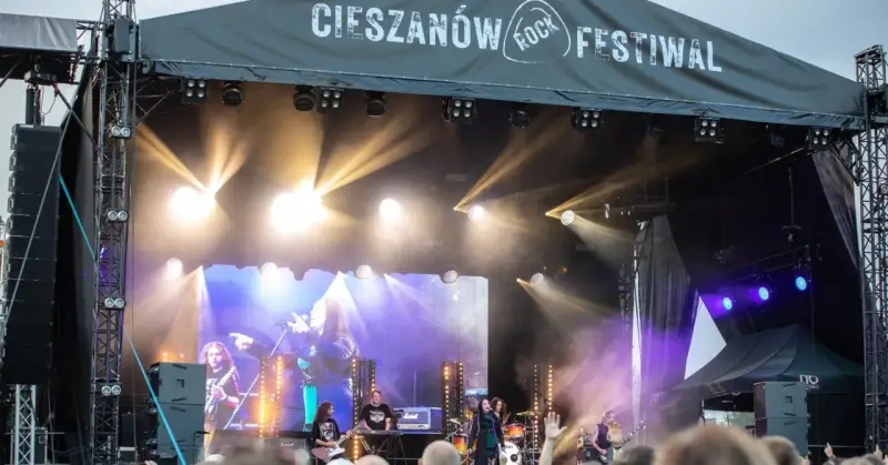 Zespół gra na scenie podczas Cieszanów Rock Festiwal. W tle wielki ekran z wizerunkiem wokalistki i reflektory.