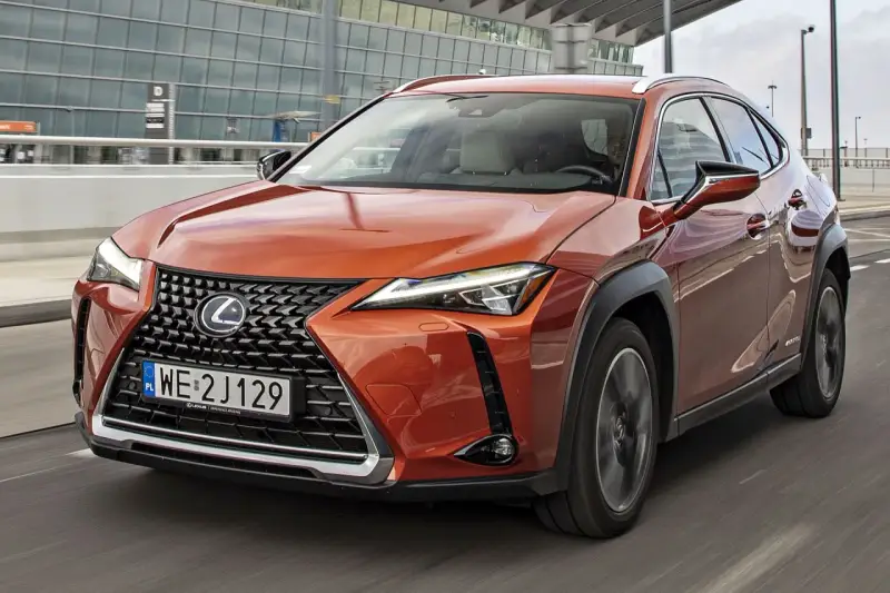 Pomarańczowy Lexus UX 250h w ruchu miejskim, z nowoczesnym grillem i reflektorami LED.
