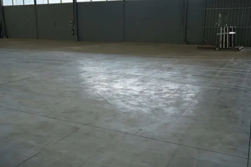 Vaste entrepôt avec une dalle béton qui part en poussière, marquée par des traces de passage.