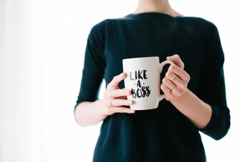Kobieta trzyma kubek z napisem "Like a boss". Czy to pewność siebie, czy tylko maska na syndrom oszusta?