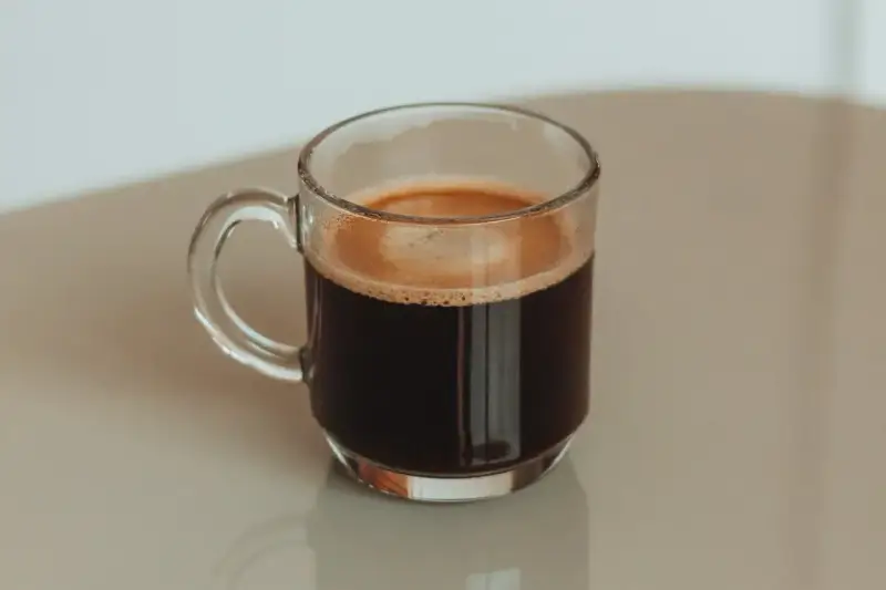 Kawa po kolonoskopii, w szklanej filiżance, z pianką na wierzchu.