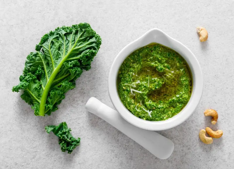 Pesto z jarmużu do słoika, gotowe do przechowywania. Obok liść jarmużu i orzechy nerkowca.
