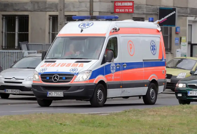 Karetka na sygnale z oznaczeniami medycznymi, jadąca ulicą.