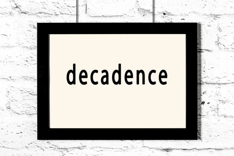 Czarny prostokątny obraz z napisem "decadence" na jasnym tle, wiszący na białej ceglanej ścianie. Symbol dekadentyzmu.