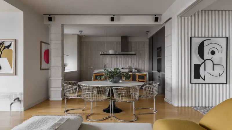 Nowoczesne wnętrze z okrągłym stołem i krzesłami w stylu bauhaus. W tle kuchnia i abstrakcyjne obrazy.