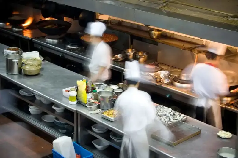 Chefs en movimiento en una cocina profesional, con ollas humeantes y ingredientes listos. El "mise en place" es clave para la eficiencia.